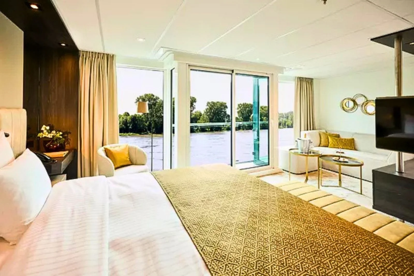 A river cruise suite with a wide bed, sitting area and sliding glass doors to a French balcony