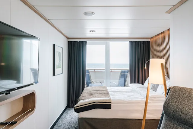 A balcony cabin with a bed and open doors to a private balcony over the water