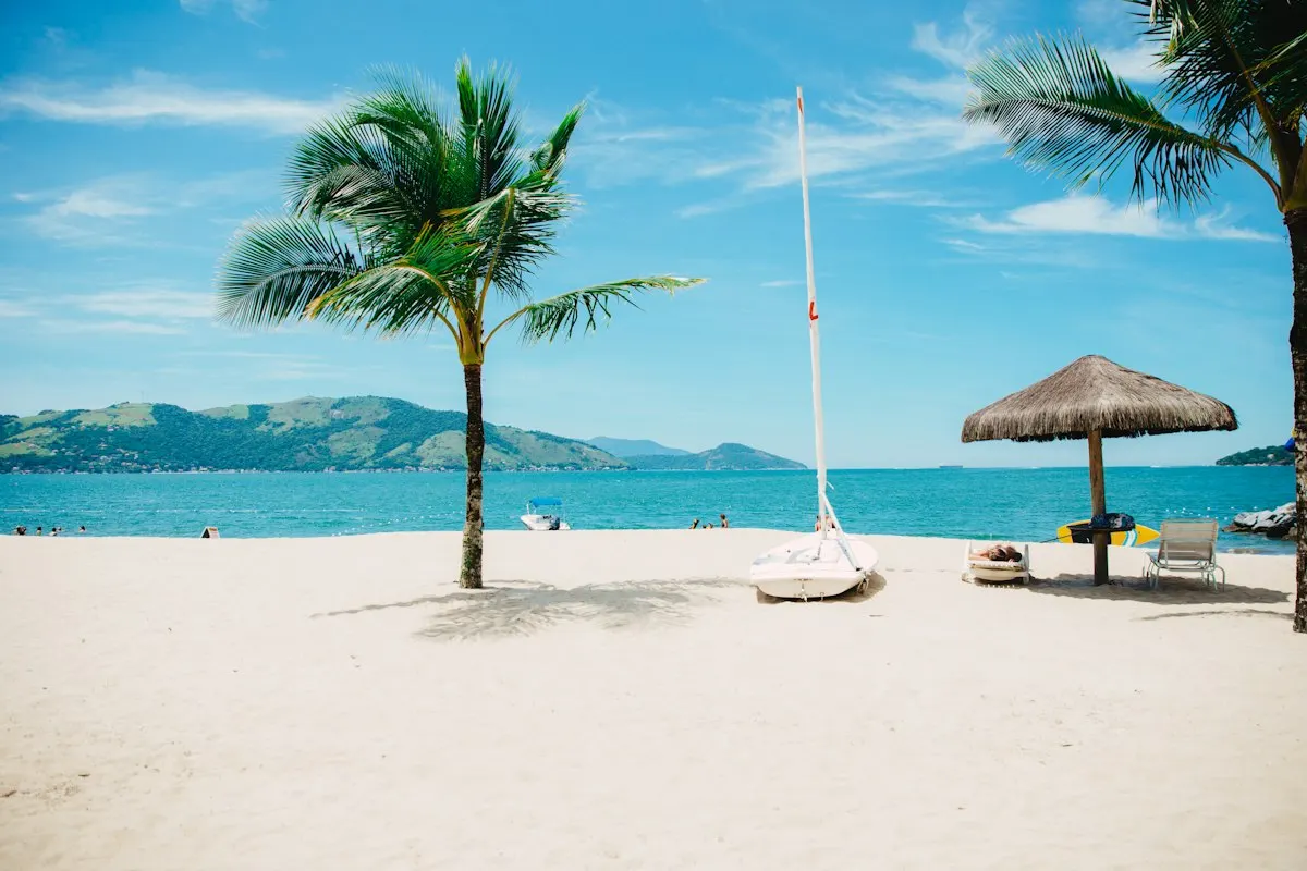 A thatched beach umbrella and loungers on white sand beside turquoise water
