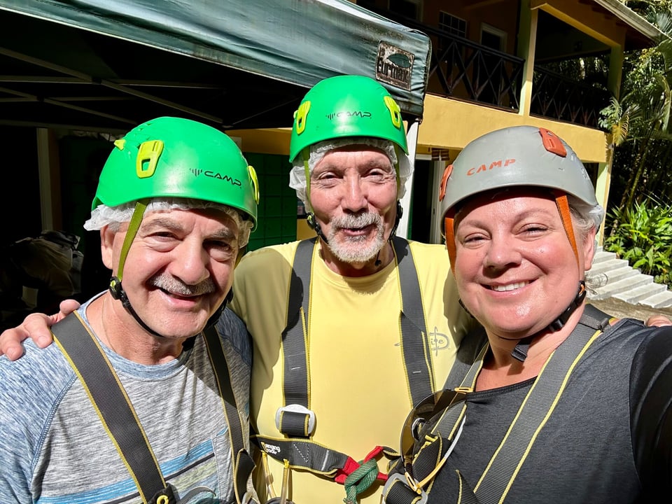 Three Journey with Erika travelers wearing helmets and zipline harnesses posing for a selfie at a jungle adventure course on their Southern Caribbean cruise