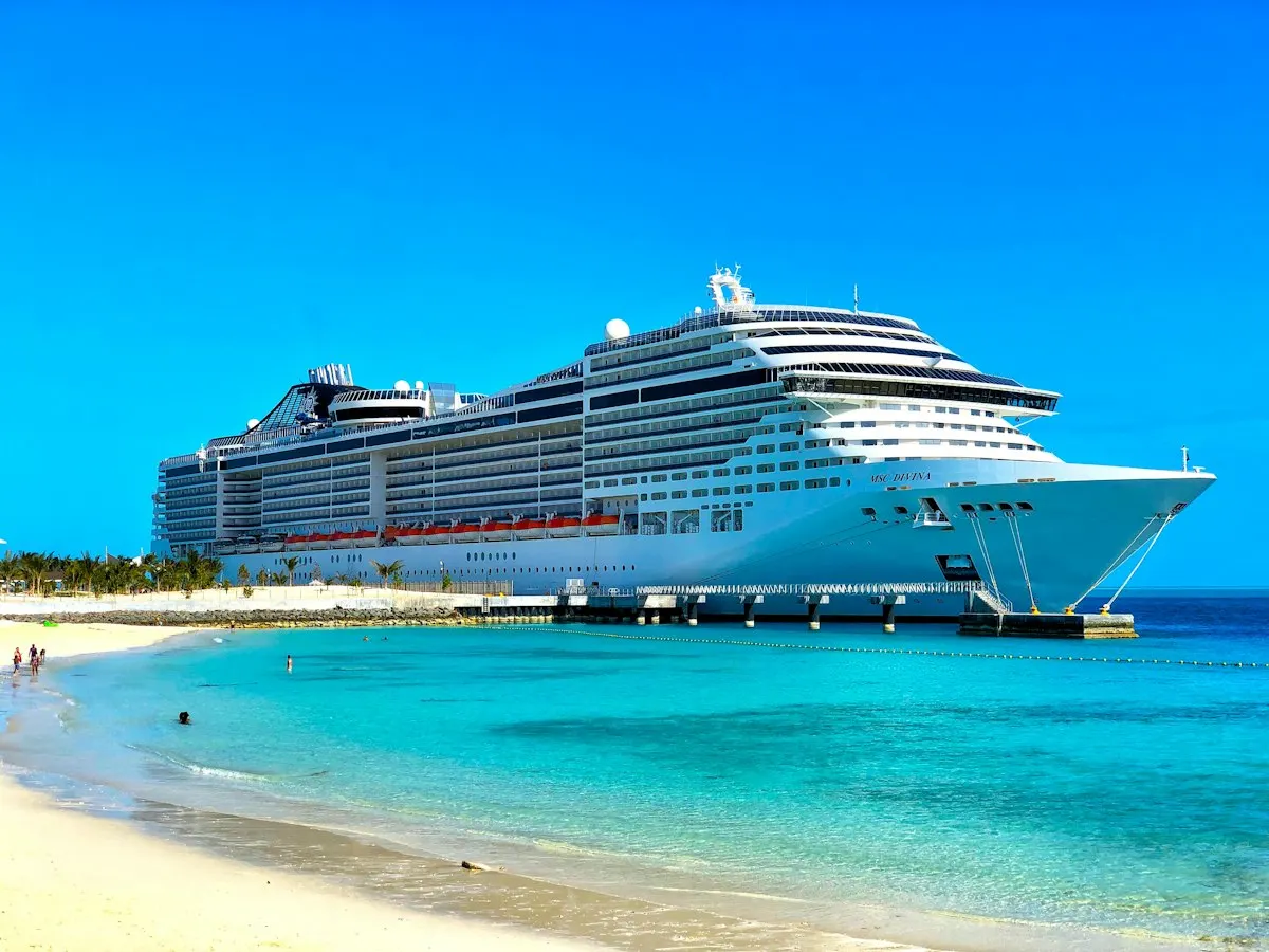 A large cruise ship docked beside a white-sand beach and clear blue water