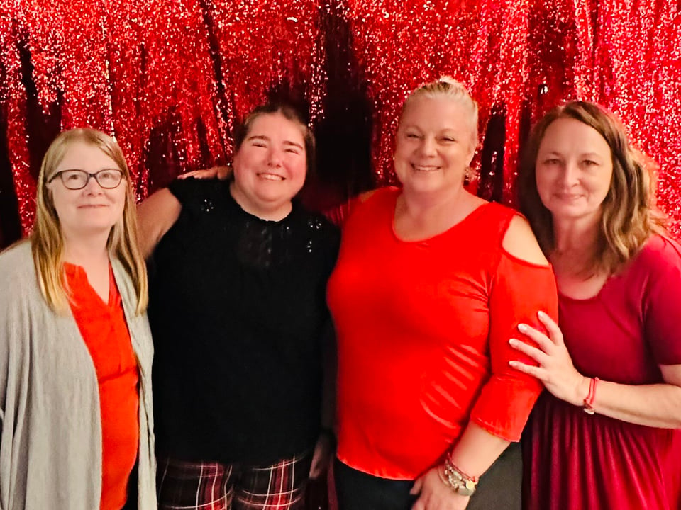 Four Journey with Erika travelers dressed in red posing together in front of a red sequined backdrop at a party aboard Scarlet Lady