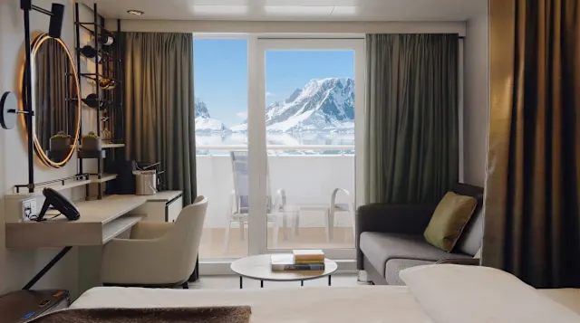A suite with a seating area and open balcony doors overlooking icy mountains in Antarctica