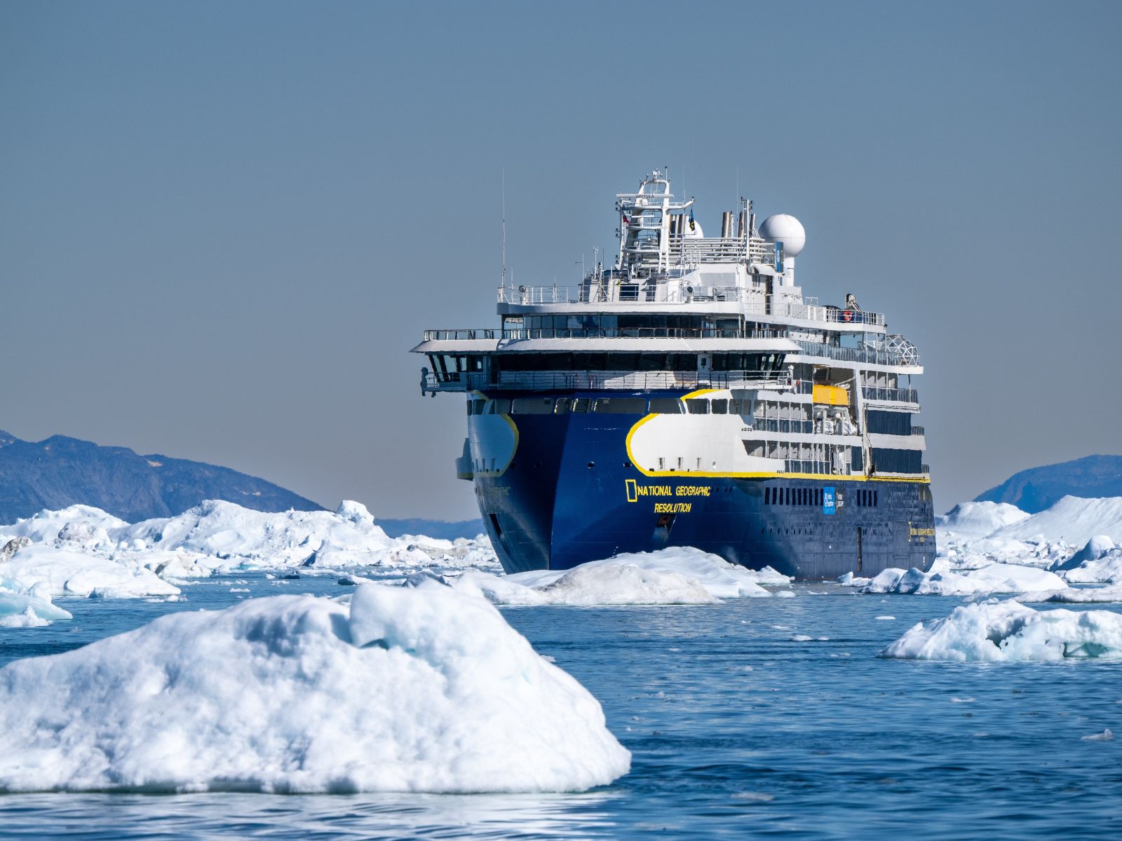 An expedition cruise ship sailing past large floating icebergs in polar water