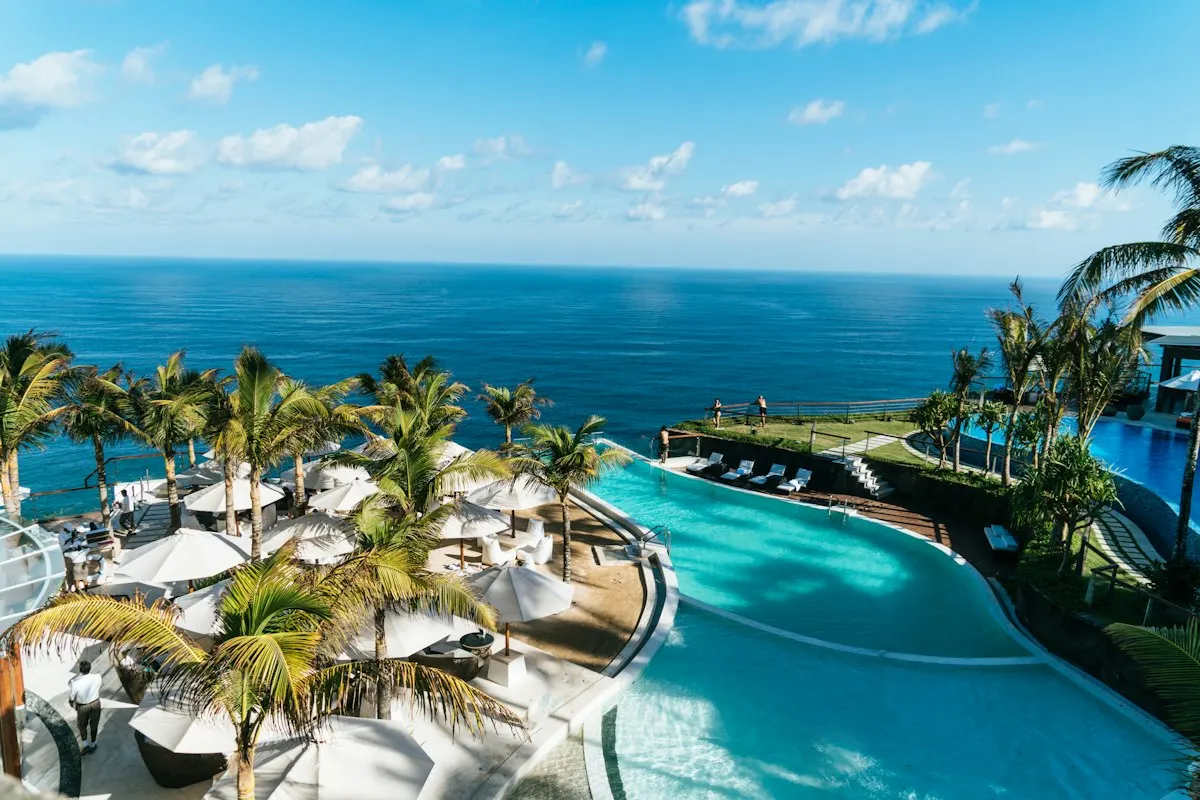 A palm-lined resort pool and beach umbrellas beside the ocean