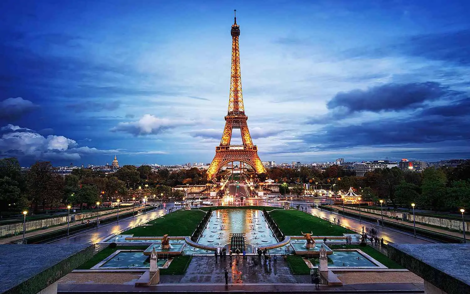 The Eiffel Tower lit up at twilight, seen from the Trocadéro gardens across the Seine