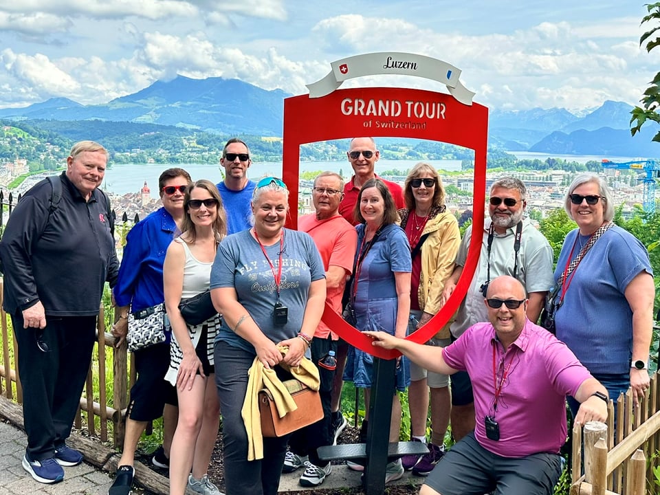 Journey with Erika travelers posing beside the red Grand Tour of Switzerland sign at a viewpoint above Lucerne and Lake Lucerne