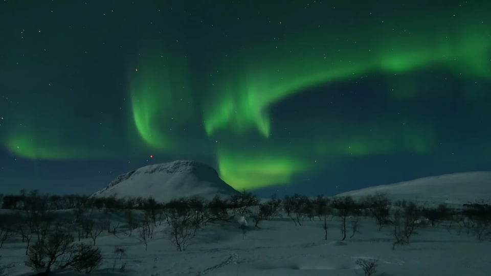 Green northern lights swirling over a snowy fell in Finnish Lapland