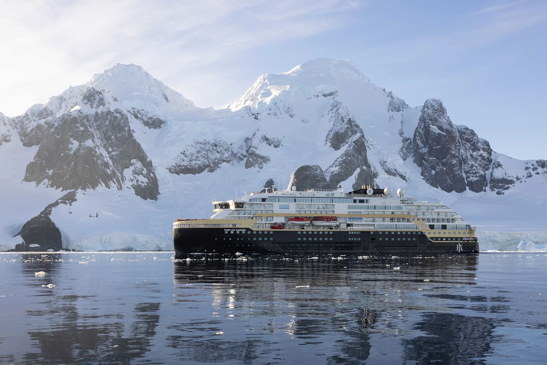 An expedition ship anchored in icy Antarctic water below snow-covered mountains
