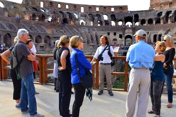 A tour guide addressing a small group of travelers inside the Colosseum in Rome