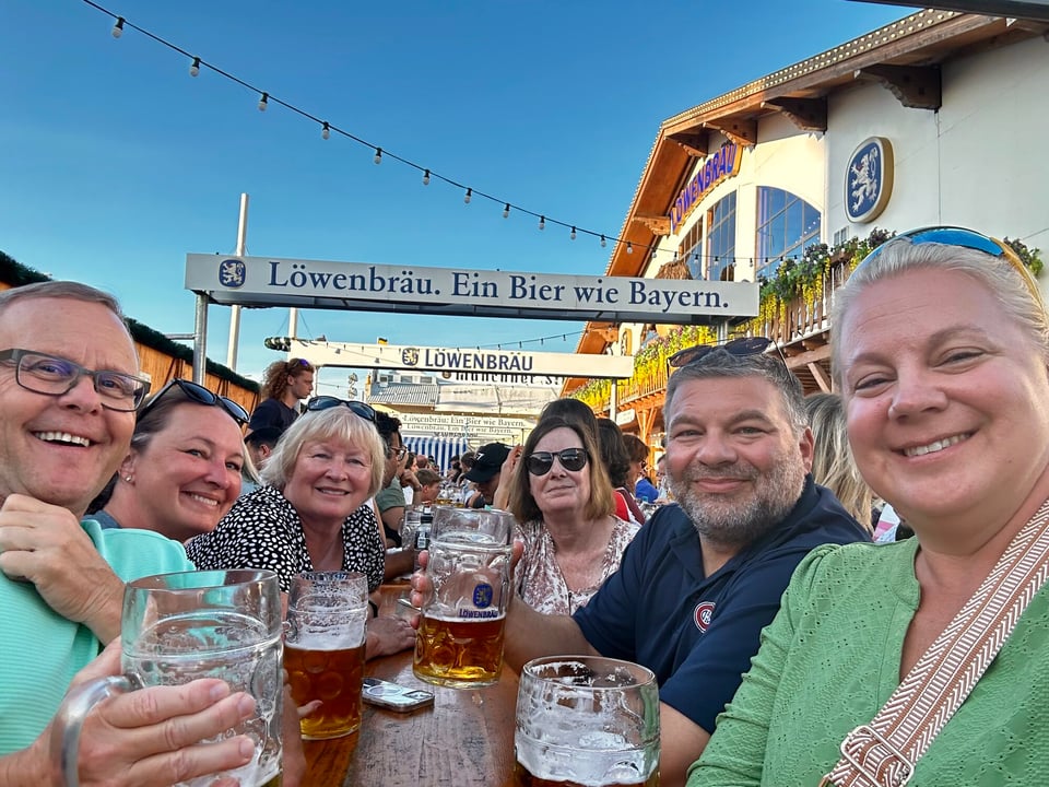 Six Journey with Erika travelers raising beer mugs together at a wooden table in the Löwenbräu beer garden at Oktoberfest in Munich