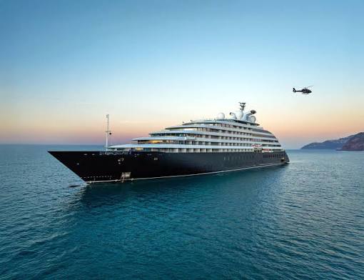 A sleek dark-hulled luxury cruise ship sailing on calm turquoise water at sunset