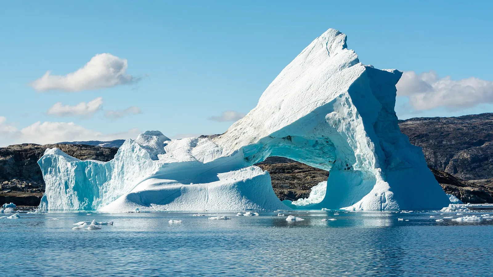 A large arched iceberg reflected in the still water of a Greenland fjord