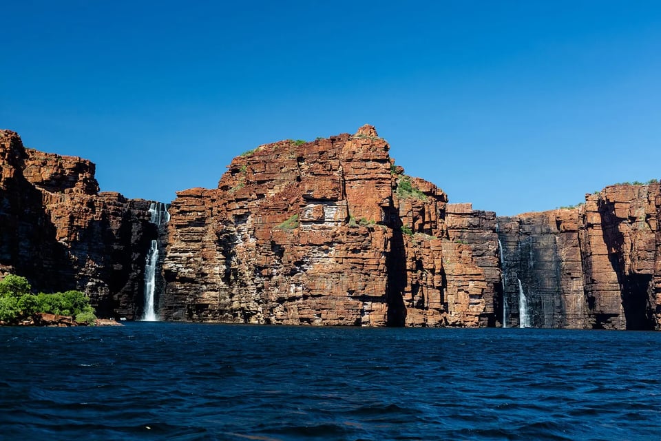 Twin waterfalls pouring over red sandstone cliffs into deep blue water at King George Falls, Kimberley
